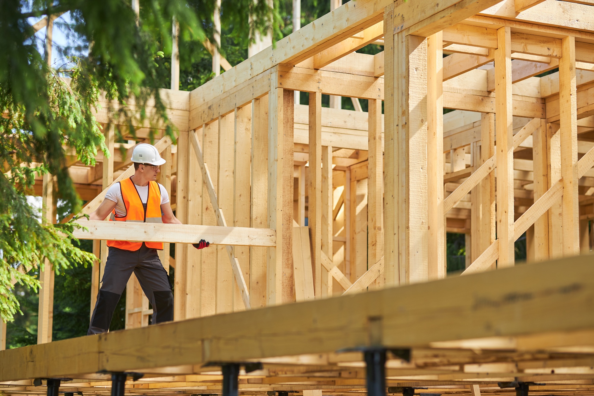 Strong builder constructing wooden house, building, wearing yellow vest and white helmet.